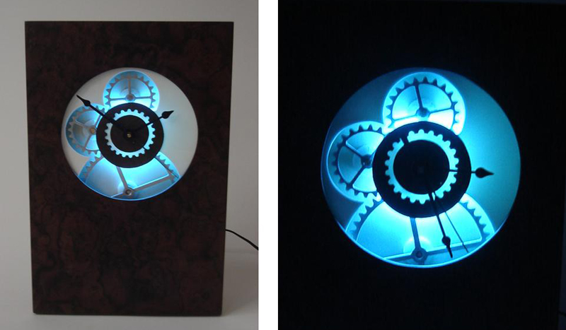 Illuminated Moving Gear Clock - Our standard moving gear clock but with a backlit face.  Both pictures are of the same clock - one in daylight and one at night.  Illuminated logos can be applied to the lower half of the clock.  Uses one AA battery and one c-cell battery, and plugs into a wall socket with a 12volt adapter, supplied with purchase.  A very cool piece of kinetic art.